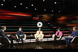 Personen diskutieren in einer TV-Talkshow-Studio-Umgebung.