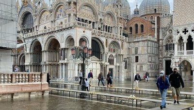 Menschen auf erhöhten Wegen vor einem historischen Gebäude bei Hochwasser in Venedig.